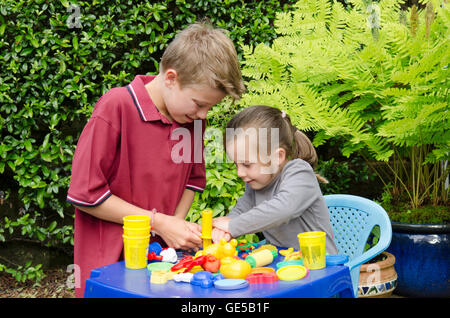 Drei Jahre alten Mädchen und Ten-Year-Old Boy, Bruder und Schwester, spielen mit Play-Doh Modellierung Kitt. VEREINIGTES KÖNIGREICH. Draußen im Garten. Stockfoto