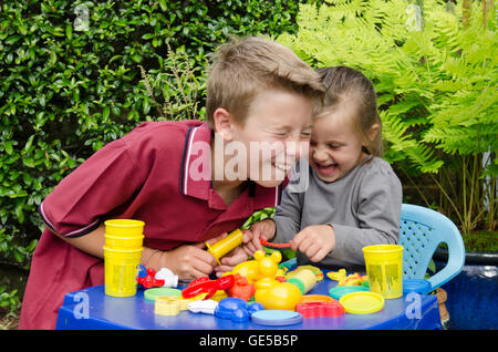 Drei Jahre alten Mädchen und Ten-Year-Old Boy, Bruder und Schwester, spielen mit Play-Doh Modellierung Kitt. VEREINIGTES KÖNIGREICH. Draußen im Garten. Stockfoto