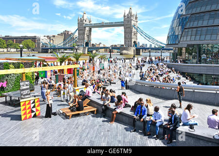 Heiße Büroangestellte und Touristen trinken im Sommer Getränke an den Imbissständen rund um Scoop im More London City Hall & Tower Bridge an der Themse Southwark UK Stockfoto