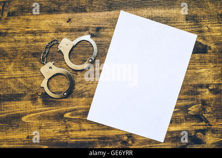 Polizeihandschellen und weißes Papier auf Ermittler Detektiv Schreibtisch, Konzept von Gesetz und Verbrechen. Stockfoto