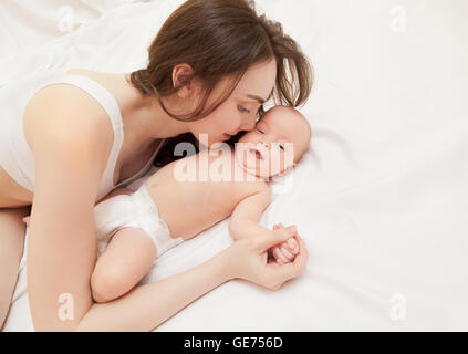 Bild der glücklichen Mutter küssen ihre entzückende Baby auf Bett liegend Stockfoto