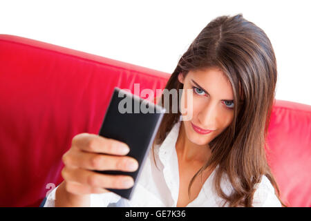 Junge Frau nehmen Selfie. Schöne Frau mit zuversichtlich Blick auf ihrem Gesicht halten Smartphone. Sie sitzt auf dem roten sofa Stockfoto