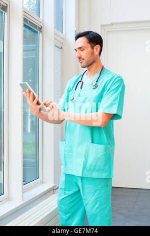 Ein Foto des männlichen Chirurgen mit digital-Tablette. Junger Arzt trägt scheuert. Er steht im Krankenhaus. Stockfoto