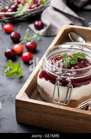 keine gebackenen Käsekuchen in ein Glas mit Kirschen auf einem schwarzen Hintergrund Beton Stockfoto