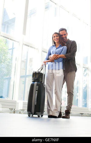 Voller Länge junger Mann umfassenden Frau von hinten am Flughafen. Porträt von liebevoller männliche und weibliche Partner sind mit dem Gepäck. T Stockfoto