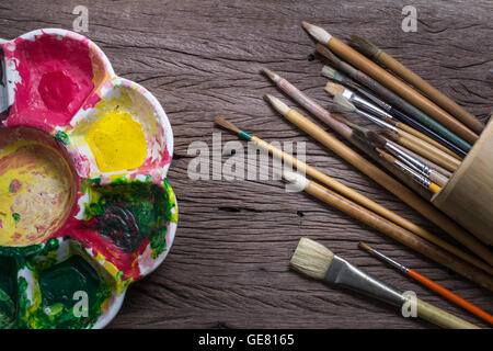 Bürsten und bunte abstrakte Farben Maler verwendet Palette auf alten hölzernen Hintergrund Stockfoto