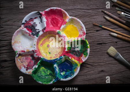 Bürsten und bunte abstrakte Farben Maler verwendet Palette auf alten hölzernen Hintergrund Stockfoto