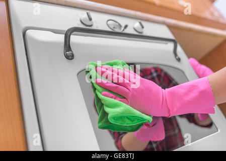 Weibliche Hände in Handschuhen gewaschen Ofen außerhalb. Reinigung der Küche. Stockfoto