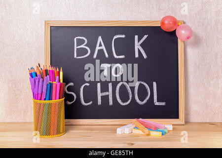 Bildungskonzept mit Text wieder in die Schule ist in Tafel, Kreide, Stifthalter, Luftballons und bunte Bleistifte auf Holz geschrieben. Stockfoto