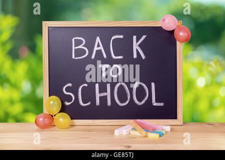 Bildungskonzept mit Text wieder in die Schule ist in Tafel, bunte Kreiden und Luftballons auf Holztisch über grüne Bok geschrieben. Stockfoto