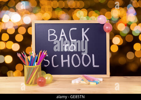 Bildungskonzept mit Text wieder in die Schule ist in Tafel, Stifthalter, bunte Kreiden und Luftballons auf Holztisch Ov geschrieben. Stockfoto