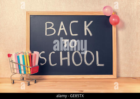 Bildungskonzept mit Text wieder in die Schule ist in Tafel, Warenkorb, Stifte, bunte Kreiden und Luftballons auf Holz geschrieben. Stockfoto