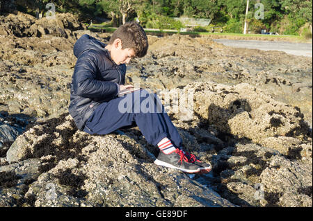 Junge auf Felsen mit mobilen Gerät Waipu Cove Stockfoto