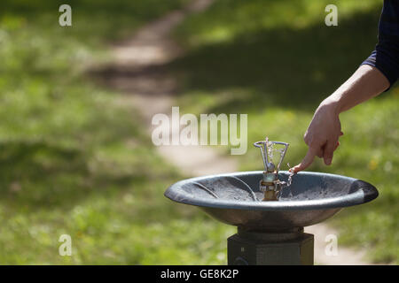 Horizontale Nahaufnahme einer Hand schob einen Metall Wasserspender in einem grünen park Stockfoto