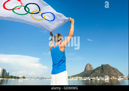 RIO DE JANEIRO - 24. März 2016: Sportler halten Olympische Flagge steht am Ufer der Guanabara Bucht am Zuckerhut. Stockfoto