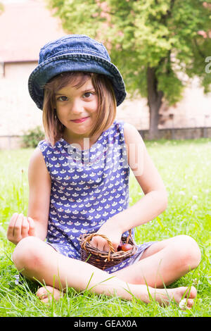 Porträt von kleinen Mädchen sitzen auf einer Wiese mit Korb von Stachelbeeren Stockfoto