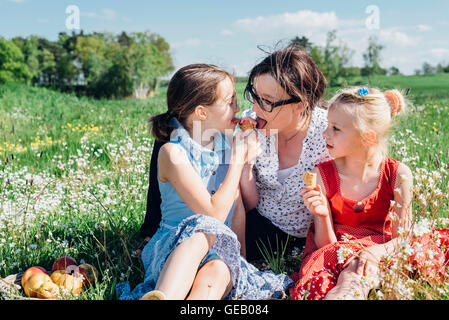 Mutter und zwei Mädchen auf Wiese essen Eiscreme-Kegel Stockfoto