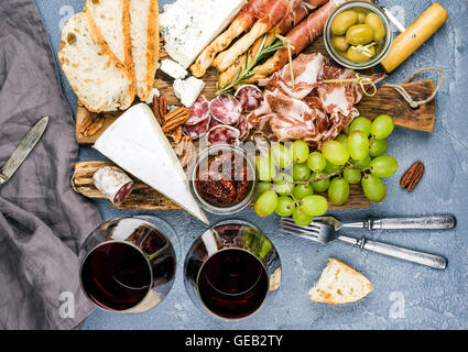 Käse und Fleisch Vorspeise Auswahl. Parmaschinken, Salami, Brot klebt, Scheiben Baguette, Oliven, getrocknete Tomaten, Trauben, Nüssen, Rotwein in Gläsern auf rustikalem Holzbrett Stockfoto