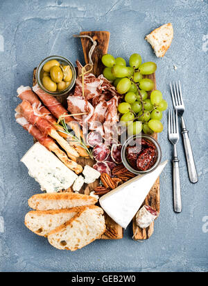 Käse und Fleisch Vorspeise Auswahl. Parmaschinken, Salami, Brot-Sticks, Baguette Scheiben, Oliven, getrocknete Tomaten, Trauben Nüssen auf rustikalem Holzbrett Stockfoto