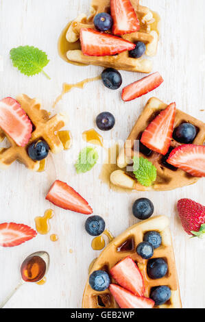 Hausgemachte belgische Waffeln serviert auf einem weißen Woodenl Tablett mit Beeren, Marple Sirup und Minze Blätter Stockfoto