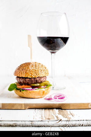 Frische hausgemachte Burger auf hölzernen servieren Brett mit Zwiebelringen und Glas Rotwein Stockfoto