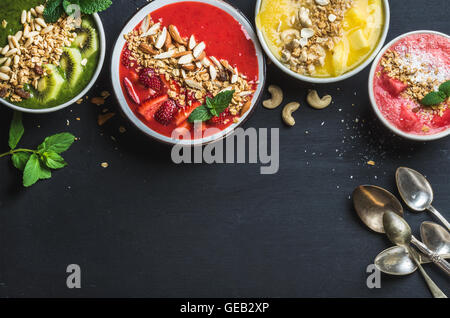 Gesunden Sommer Frühstück Konzept. Bunte Obst Smoothie Schalen mit Nüssen und Hafer-Müsli auf schwarzem Hintergrund Stockfoto