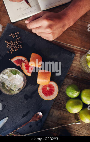 Draufsicht der Zutaten für einen Cocktail mit Barkeeper Notizen zu machen. Schneiden Sie Grapefruit und schwarzen Pfeffer mit einem vollen Glas Stockfoto