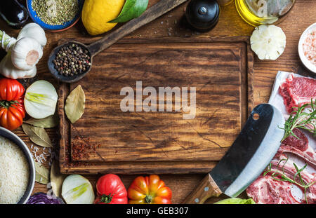 Zutaten für gesundes Fleisch Abendessen kochen. Roh, ungekocht Lammkoteletts mit Gemüse, Reis, Kräuter und Gewürze über rustikalen hölzernen Hintergrund, dunkel, Schneidebrett in Mitte Stockfoto