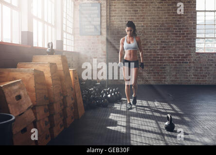 Voller Länge Aufnahme Fitness Frau zu Fuß in die Turnhalle mit Wasserkocher Glocke am Boden. Aufwärmen vor einem intensiven Fitne Sportlerin Stockfoto