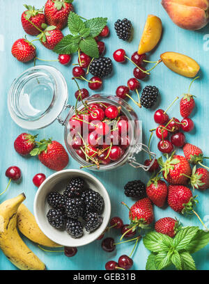 Gesunden Sommer Obstsorte. Süße Kirschen, Erdbeeren, Brombeeren, Pfirsiche, Bananen und Minze Blätter auf blauem Hintergrund Stockfoto