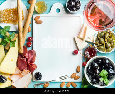 Sommerwein snack Set. Glas Rose, Fleisch, Käse, Oliven, Honig, Brot-Sticks, Nüssen, Kapern und Beeren mit keramischen Tafel im Zentrum, blauen hölzernen Hintergrund Stockfoto