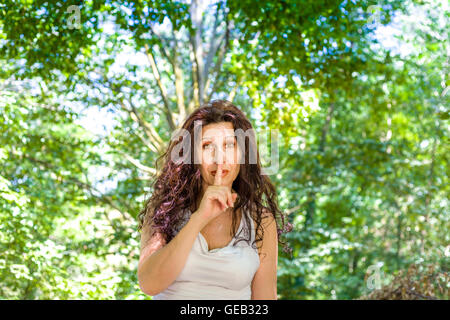 Kurvige edel Reife Frau verleiht Zeigefinger Lippen fordern Stille in einem Garten Stockfoto