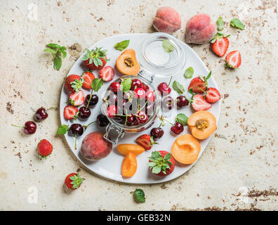 Gesunden Sommer Obstsorte. Süße Kirschen, Erdbeeren, Brombeeren, Pfirsiche, Bananen und Minze Blätter auf blauem Hintergrund Stockfoto