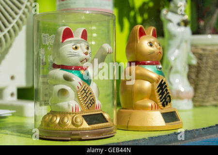 Maneki Neko (japanische verlockende Katzen) in hellem Sonnenlicht auf rotem Grund. Stockfoto