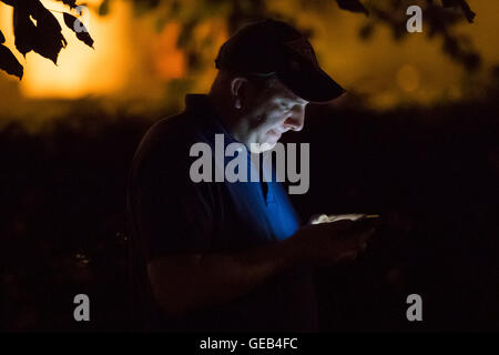 Ein Mann spielt Pokemon gehen auf seinem Handy in der Nacht. Stockfoto
