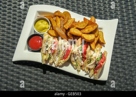 Chicken Clubsandwich mit Land Pommes auf einem Teller mit Senf und Ketchup. Stockfoto