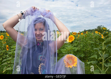 Schöne dunkelhaarige junge Frau trägt lila Tüll und stehend in Sonnenblumen Stockfoto