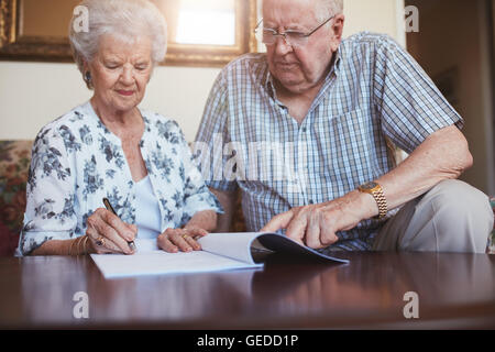 Porträt von senior Ehemann und Ehefrau zu Hause Papierkram zusammen zu machen. Ehepaar im Ruhestand Signieren von Dokumenten. Stockfoto