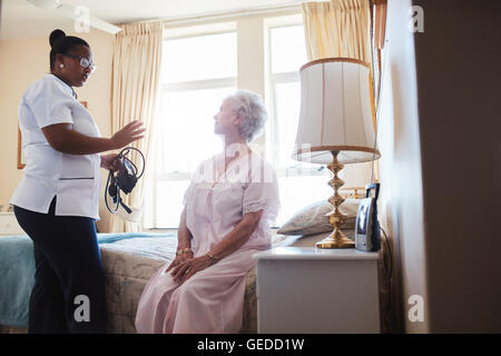 Im Innenbereich erschossen Sie nach Hause Bezugsperson im Gespräch mit senior Frau sitzt auf dem Bett. Ärztin, die ihre älteren Patienten zu Hause besuchen. Stockfoto