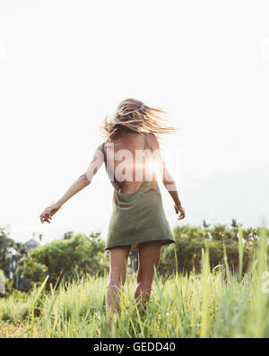 Rückansicht Schuss einer jungen Frau im Feld mit Sonne Flare. Schöne Frau im Sommerkleid in einer Sommerwiese. Stockfoto