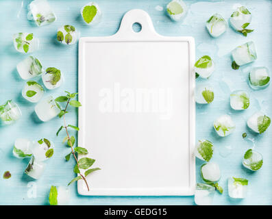 Eiswürfel mit gefrorenen Minze innen blau türkis Hintergrund und weißer Keramik Board im Zentrum, Textfreiraum Stockfoto