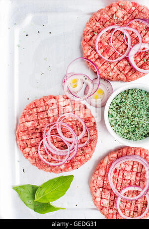 Drei roh Boden Rindfleisch Fleisch Schnitzel, Burger mit Zwiebelringen und Gewürzen auf weißen hölzernen Hintergrund, Ansicht von oben Stockfoto