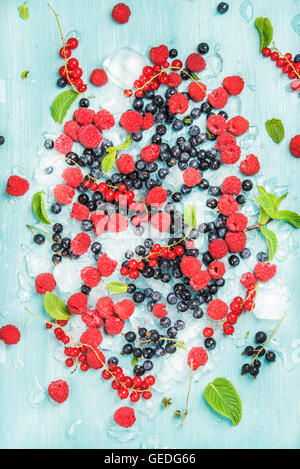 Frischen sommerlichen Garten Beerensorten. Himbeer, schwarze und rote Johannisbeeren, Bilberrry, Minze auf zerstoßenem Eis auf blauem Hintergrund Stockfoto