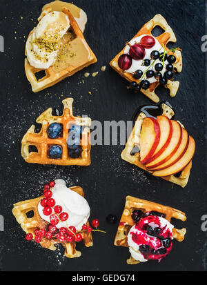 Warme hausgemachte Waffeln mit frischen Garten Beeren, Obst und Eis auf dunklem Schiefer Stein Stockfoto