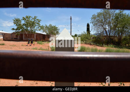 Eine Lücke in der aktuellen Metal Grenzmauer zeigt Jugendliche in Mexiko und die ursprüngliche konkrete Grenzstein in Naco, Arizona, USA. Stockfoto