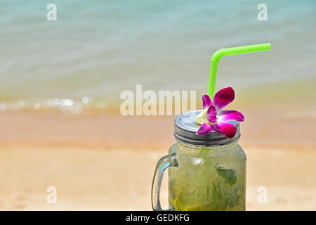 Große Gläser Becher Stil vollen Glas frisch gefrorenen Mojito mit Metallkappe Deckel, Stroh und lila Orchidee Blume im Café am Strand Stockfoto