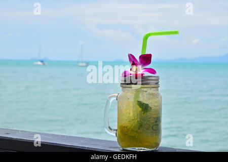 Große Gläser Becher Stil vollen Glas frisch gefrorenen Mojito mit Metallkappe Deckel, Stroh und lila Orchidee Blume im Café am Strand Stockfoto