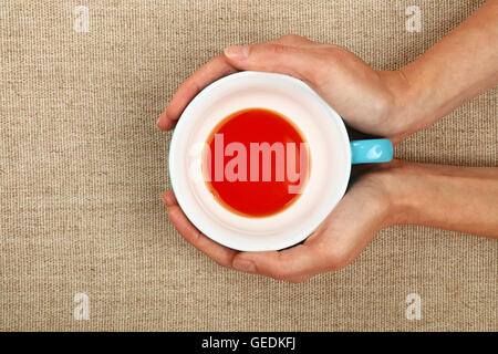 Zwei Frau Hände halten, umarmen großen leeren fertigen blaue Tasse rote Schwarztee über Leinwand Hintergrund, Hände wärmend Stockfoto