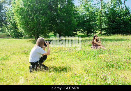 Fotograf nimmt eine Frau sitzen auf dem Rasen im Park am Sommertag Stockfoto