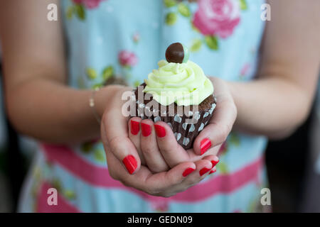 Nahaufnahme Bild von einer Frau Hände halten einen braunen Cupcake mit Minze Zuckerguss gekrönt. Stockfoto